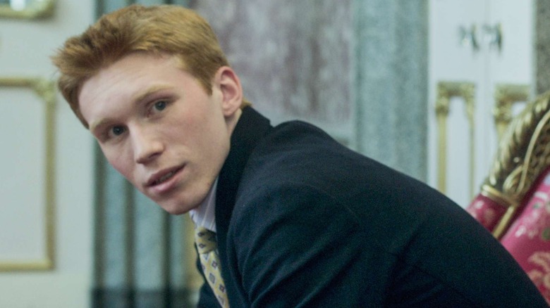 Luther Ford as Harry wearing a suit and sitting down in The Crown