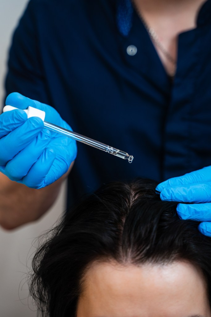 Trichologist applying scalp serum to a person's hair.