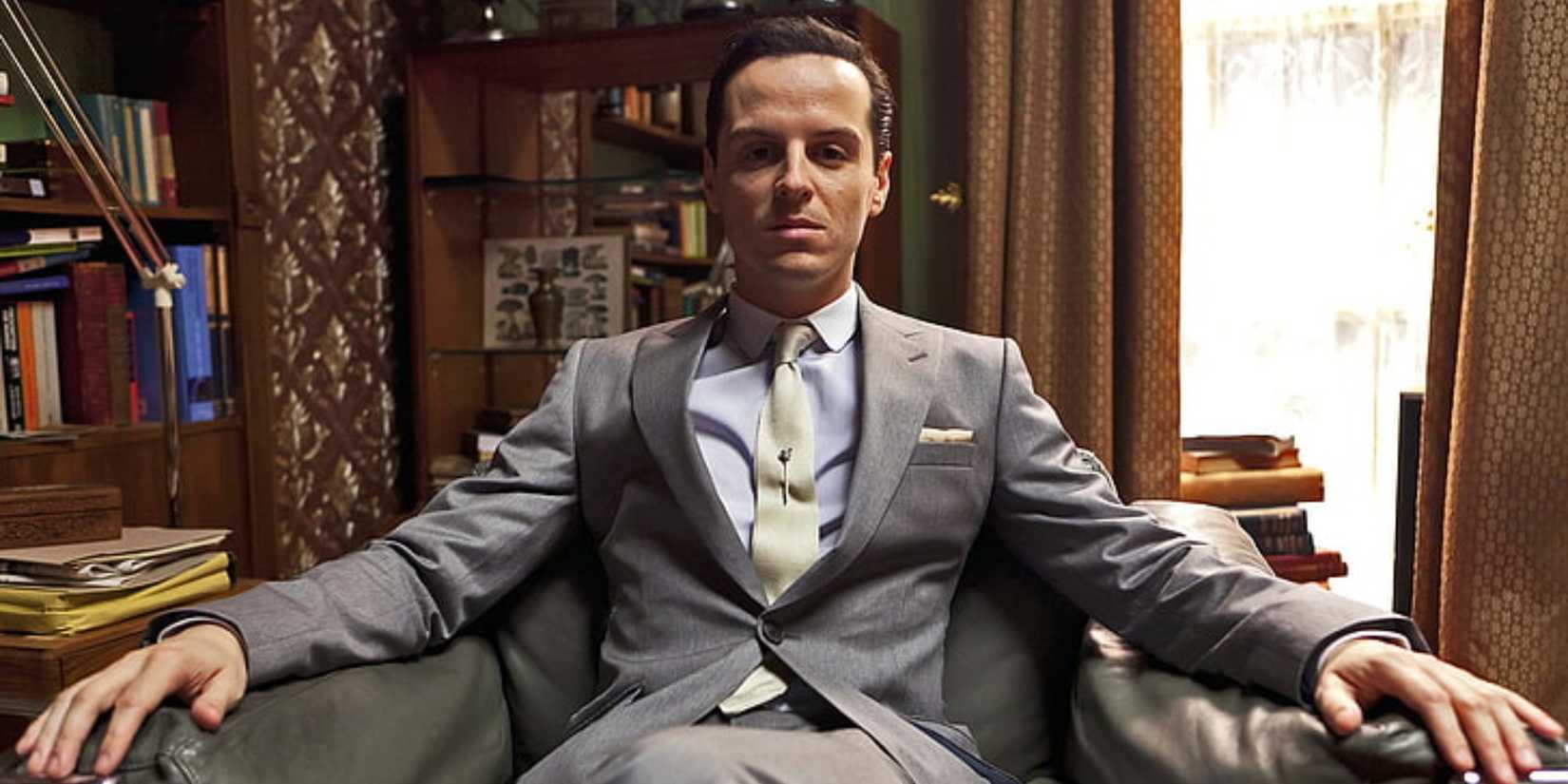 Andrew Scott as Jim Moriarty sitting in Sherlock's living room, staring straight into the camera, in Sherlock.
