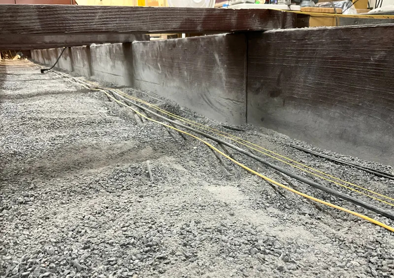 A photo of yellow and black wires laid on top of a grayish rocky surface next to a cement wall.