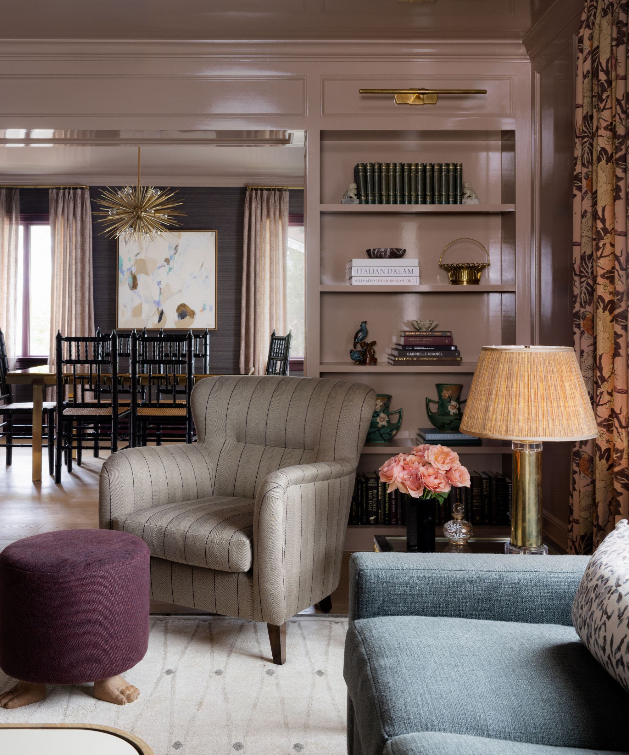 A formal living room with plaster pink walls and built-ins in a gloss finish. A powder blue sofa, a taupe armchair, and a purple footstool.