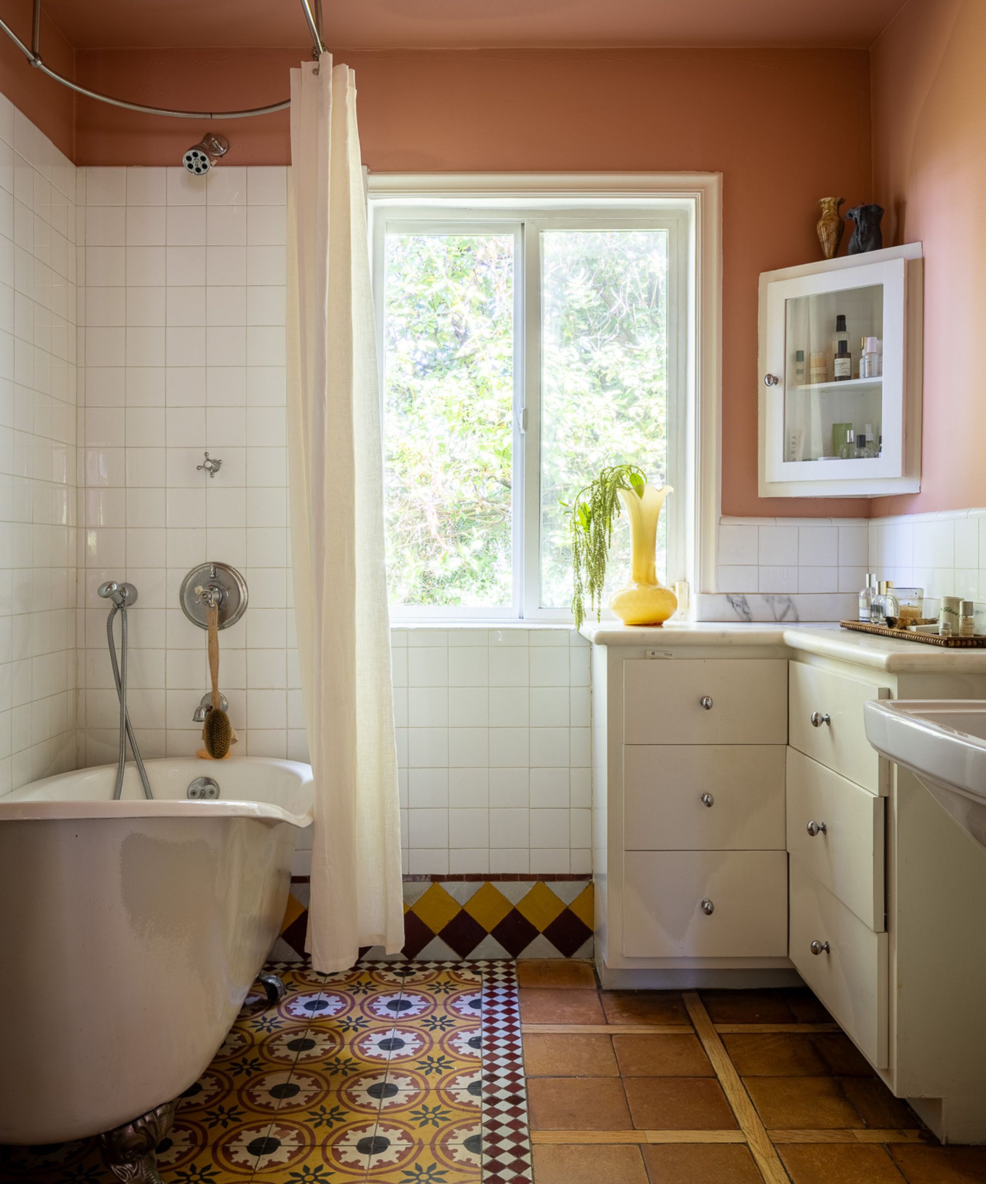 A bathroom with terracotta walls, white tiles, mustard tiled flooring and white fixtures.