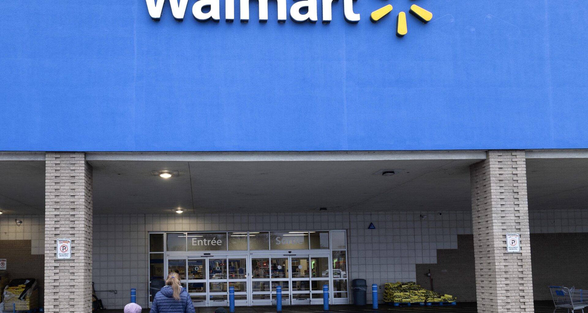 An adult and two children walk toward a Walmart entrance.