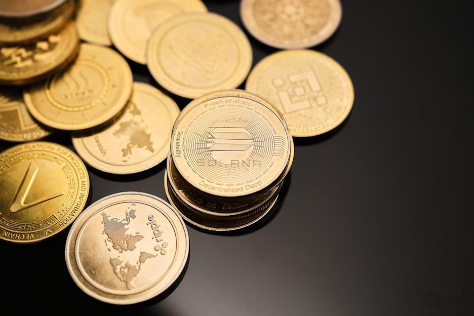 Cryptocurrency gold coins with different designs highlighting Solana are scattered on a shiny black surface, displaying a mix of symbols and names linked to digital currencies.