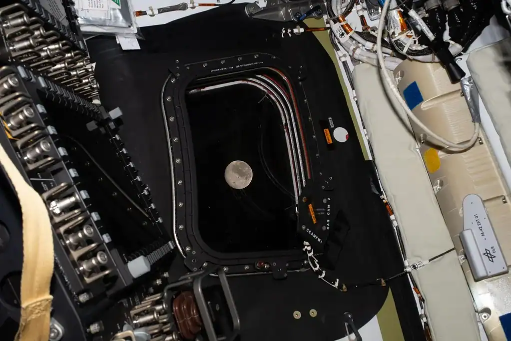 Spacecraft interior with instrumentation and the moon visible through the window.