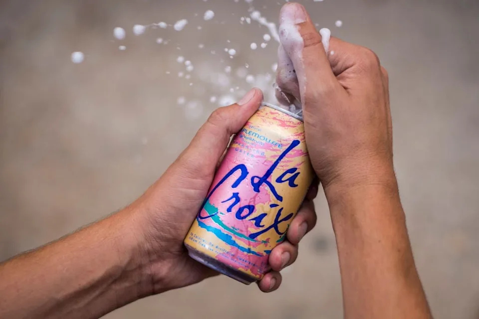 Hands opening a can of LaCroix sparkling water, with liquid bursting out, capturing the refreshing and effervescent moment