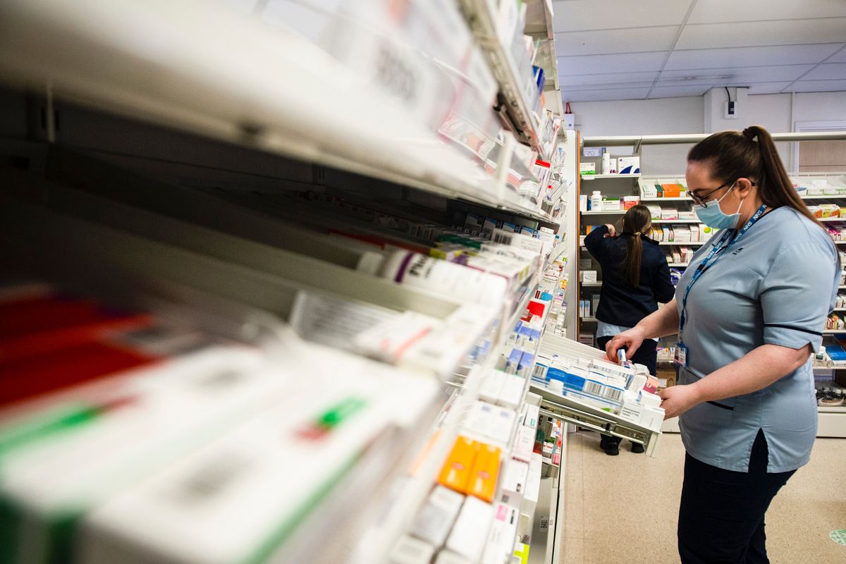 A trainee pharmacy staff member puts in order medications in drawers and shelves 
