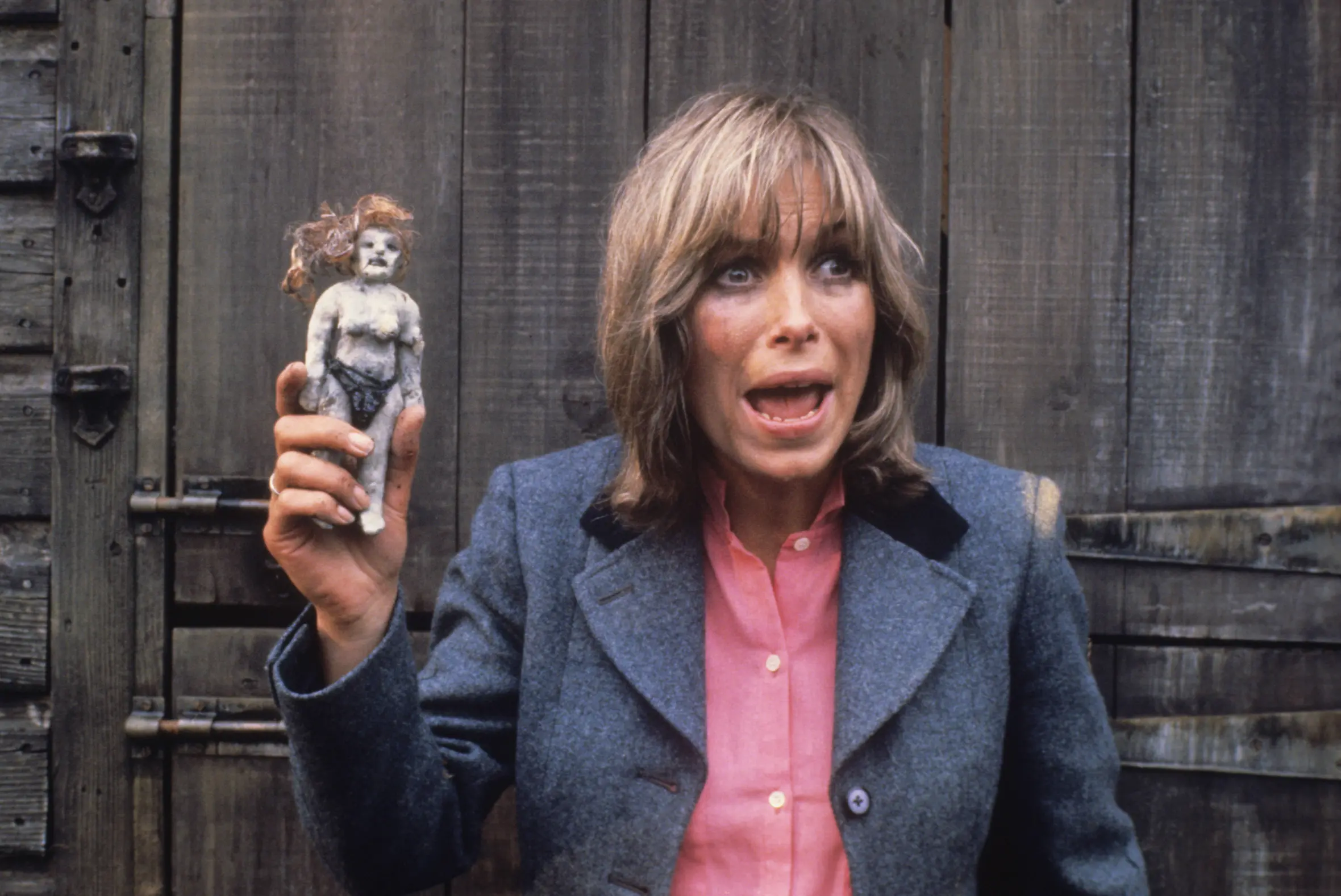 Prunella Gee, with a shocked expression, holding a doll with orange hair.