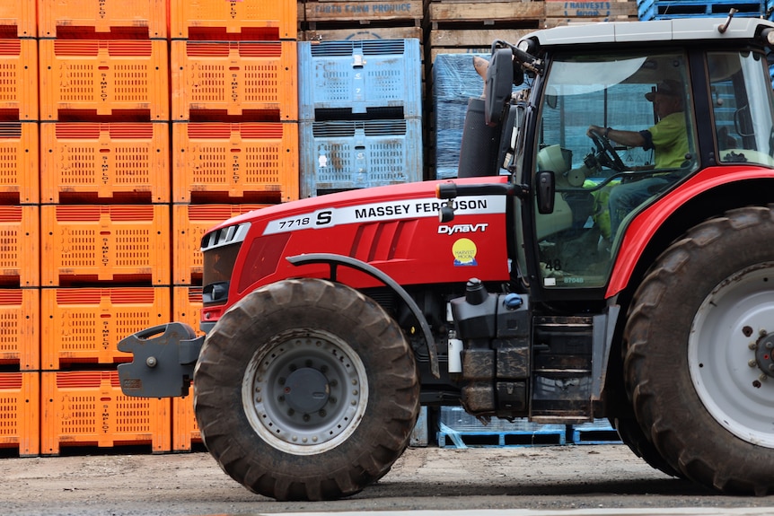 a red tractor drives in front of rows of vegetable pallets