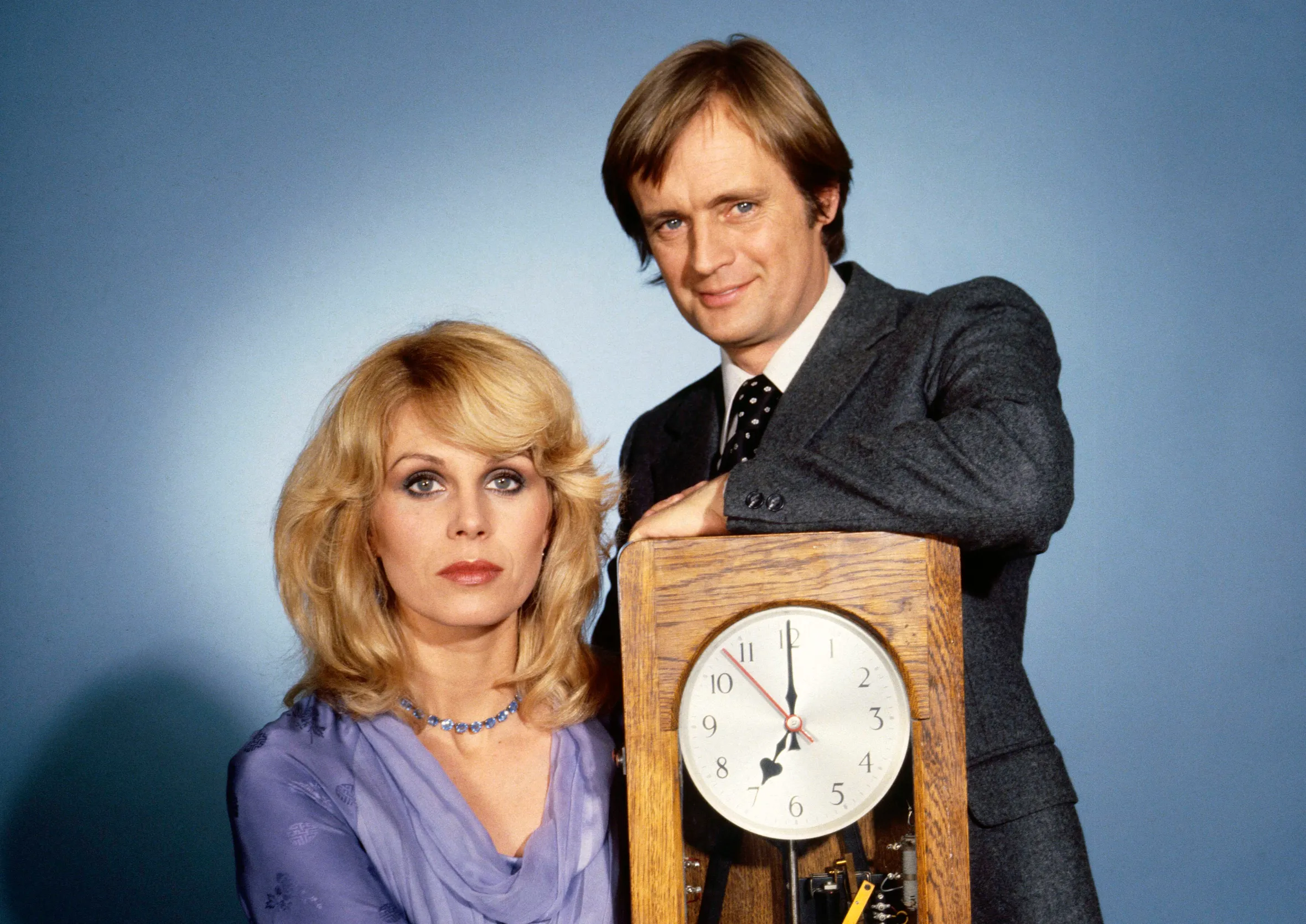Joanna Lumley as Sapphire and David McCallum as Steel with a grandfather clock, against a blue background.