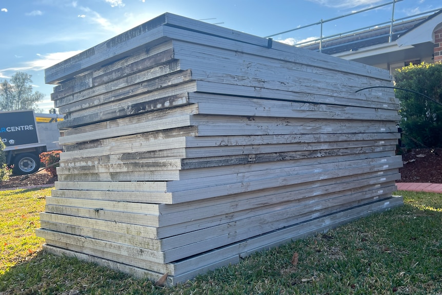A large stack of silver-framed solar panels on a patch of green grass.