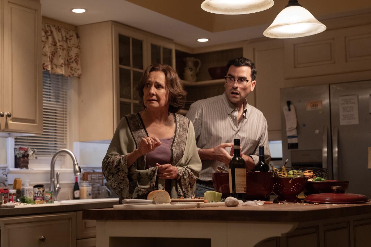 A woman and a man stand at a kitchen island covered in cutting boards and other kitchen utensils.