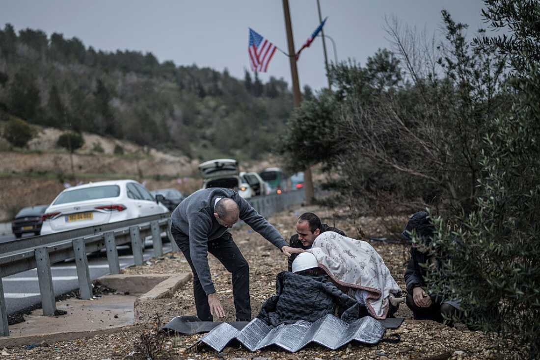 A man holds in place a protective helmet on the head of a child as other motorists take shelter from an incoming missile attack in a ditch on the side of the highway in Latrun, Israel, on Wednesday.