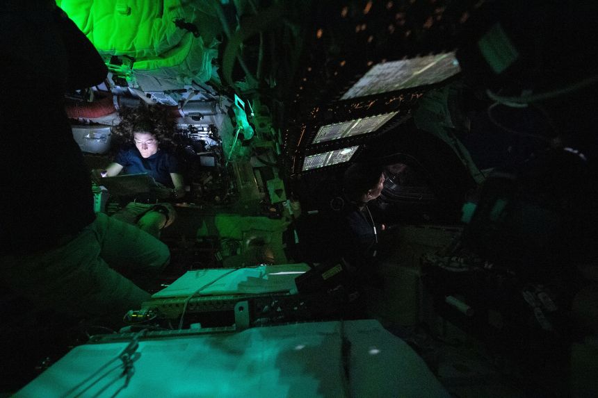 NASA astronaut Christina Koch reads on a tablet in the Orion crew capsule on Friday while astronaut Jeremy Hansen (center right) looks out of one of Orion’s windows.