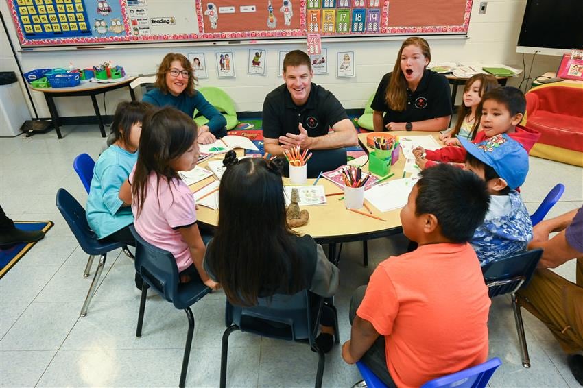 3 adults sit with children at school table 