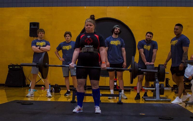 A woman holds a barbell as she competes in a powerlifting competition.