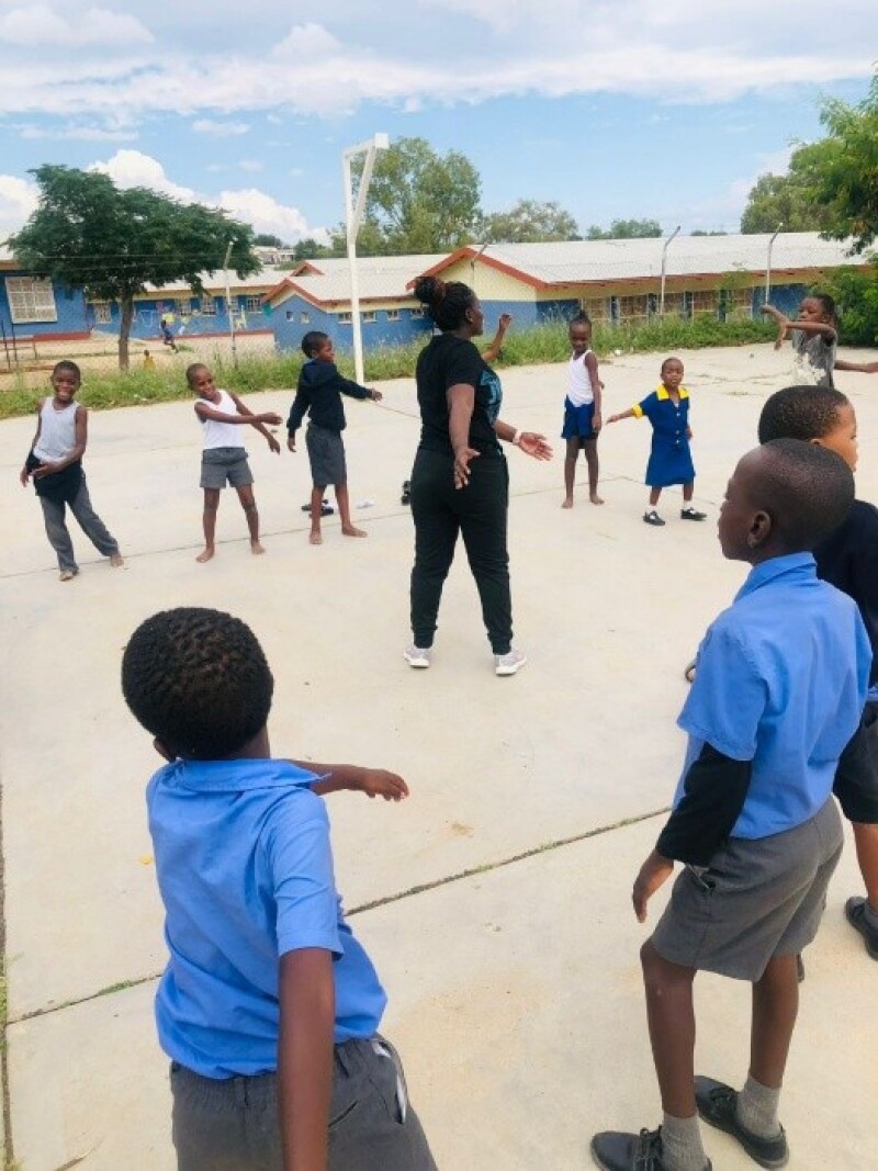 A coach stands in the middle of a circle while athletes around her follow her stretching directions. 