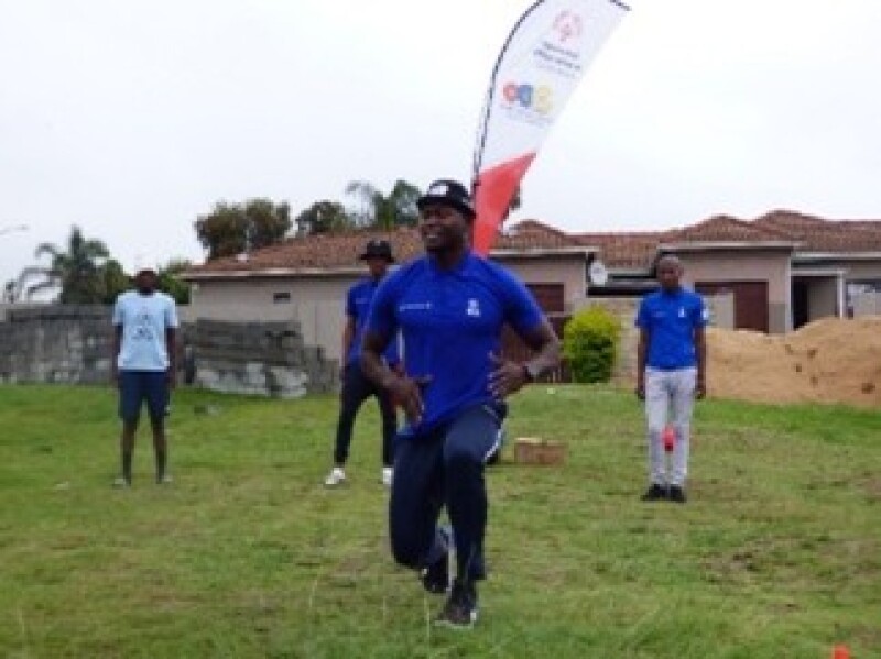 A man demonstrates a fitness activity to a group of people outside. 