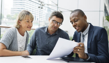 A man and a woman look at a paper that another man is showing them.