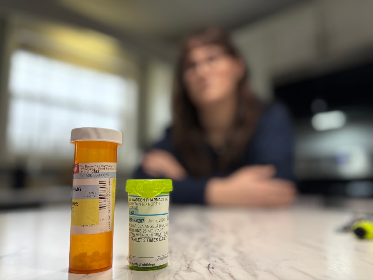 A blurred woman sits behind two pill bottles.