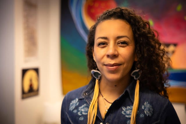 Woman with black and flowered top and dark curly hair looks into the camera