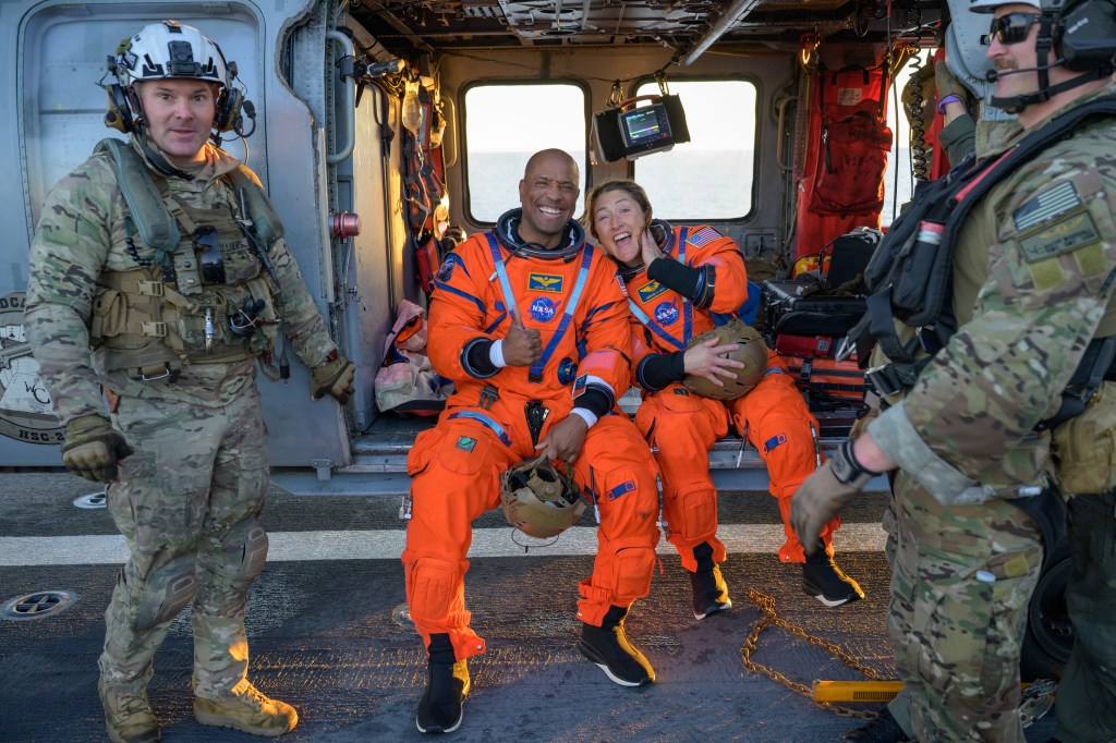 NASA astronaut Victor Glover, Artemis II pilot, left, and NASA astronaut Christina Koch, Artemis II mission specialist are seen sitting on a Navy MH-60 Seahawk from Helicopter Sea Combat Squadron (HSC) 23 on the flight deck of USS John P. Murtha after they and fellow crewmates CSA (Canadian Space Agency) astronaut Jeremy Hansen, Artemis II mission specialist, and NASA astronaut Reid Wiseman, Artemis II commander, were extracted from their Orion spacecraft after splashdown, Friday, April 10, 2026, in the Pacific Ocean off the coast of California. NASA’s Artemis II mission took the quartet on a nearly 10-day journey around the Moon and back to Earth. Following a splashdown at 5:07 p.m. PDT (8:07 p.m. EDT), NASA, U.S. Navy, and U.S. Air Force teams are working to bring the Orion spacecraft aboard the recovery ship.