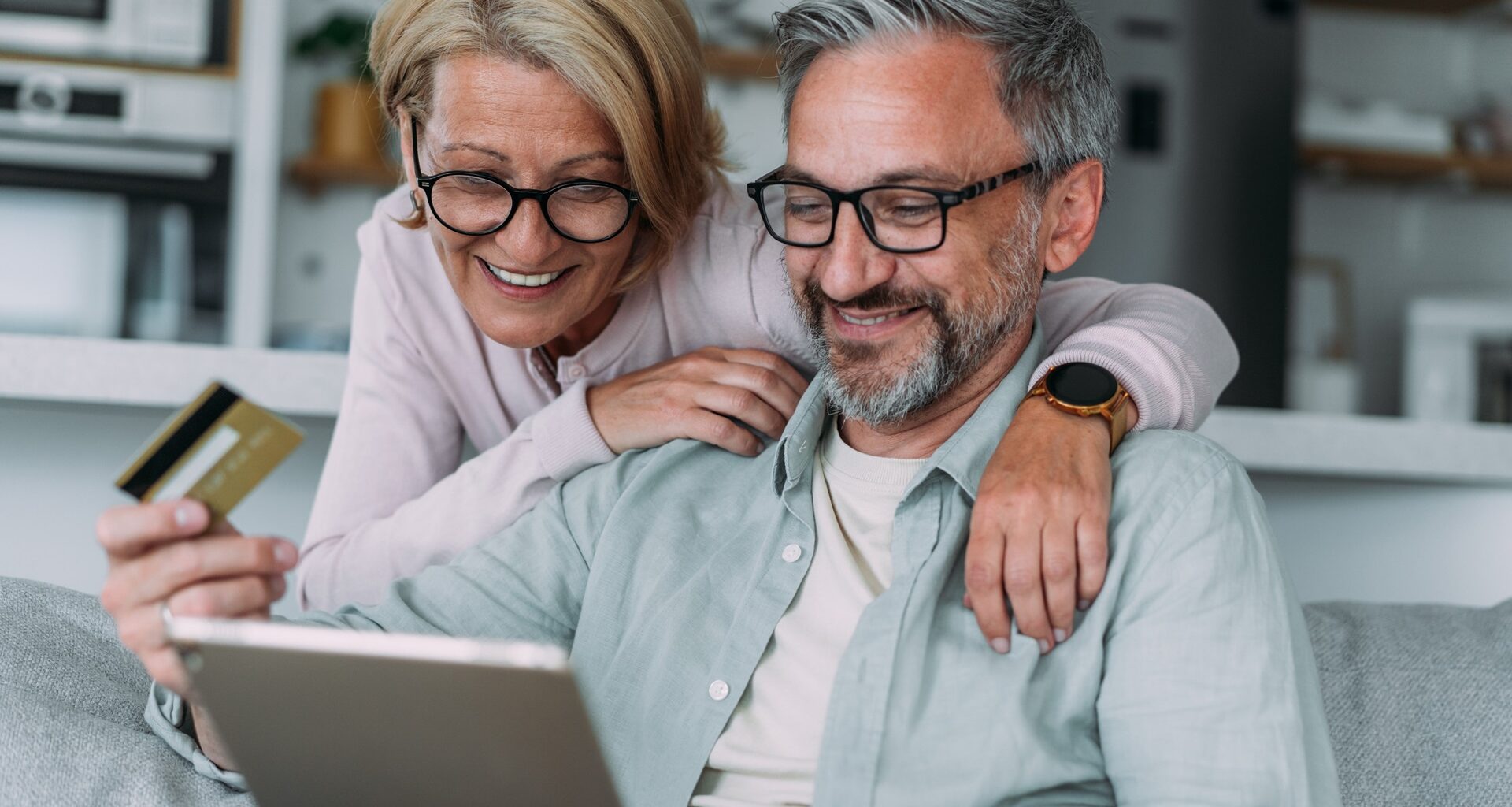 A happy older couple at home together, using tablet for online shopping.