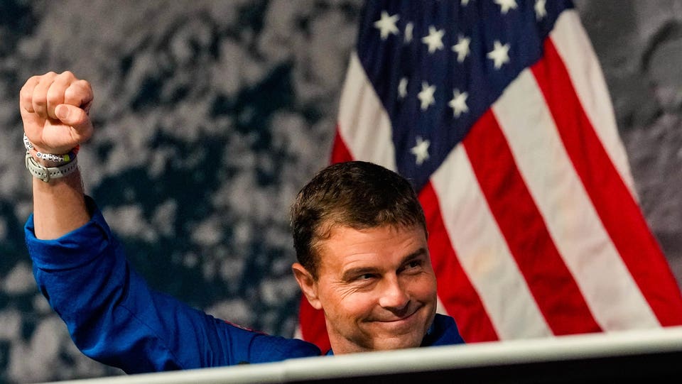 Artemis II Commander Reid Wiseman giving a triumphant fist raise, and the American flag and the Moon's surface behind him, representing the essential leadership skill for 2026 as shared by Rachel Wells in Forbes