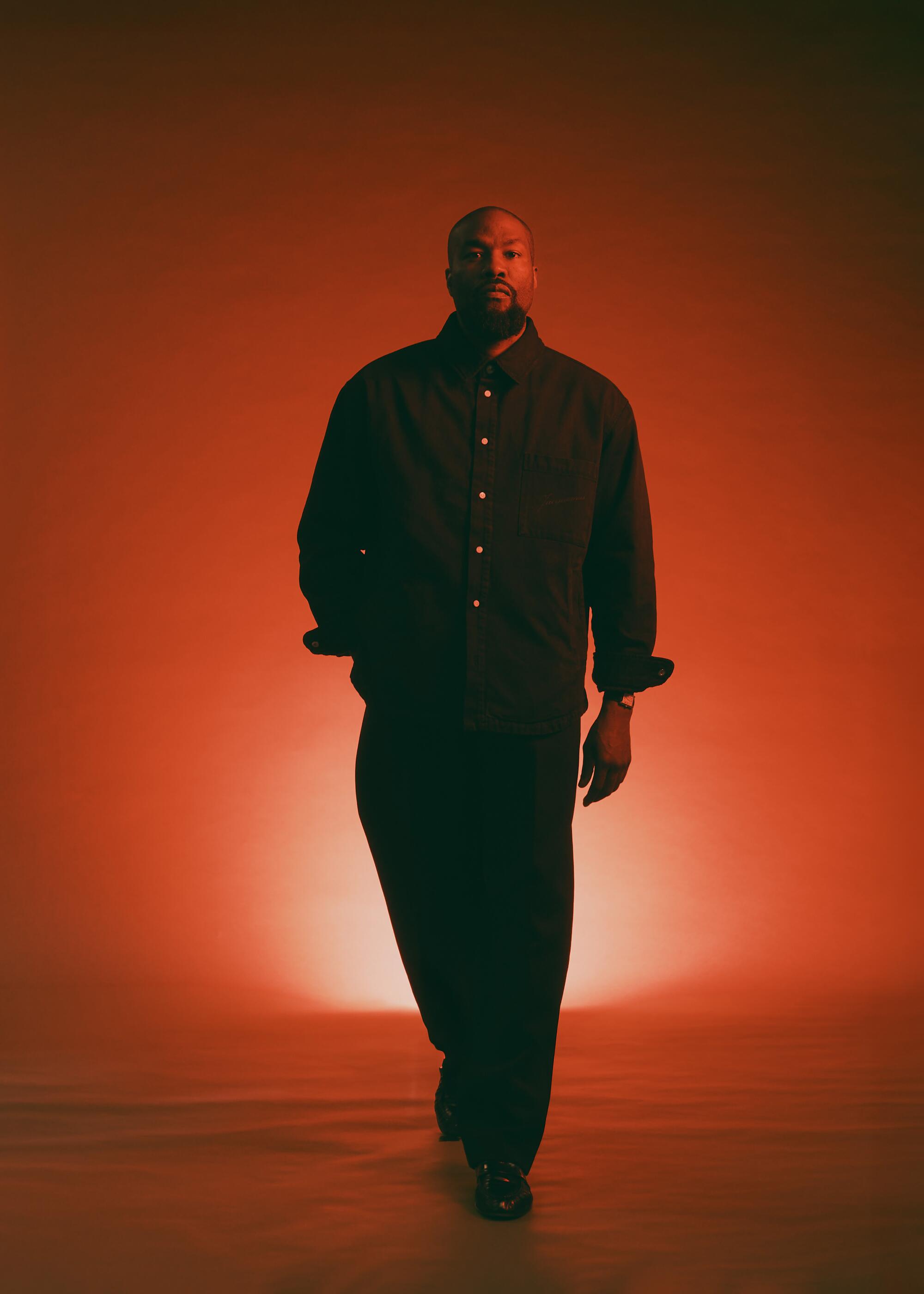 A man in a dark long-sleeve shirt and pants midstride in a red-lit room.