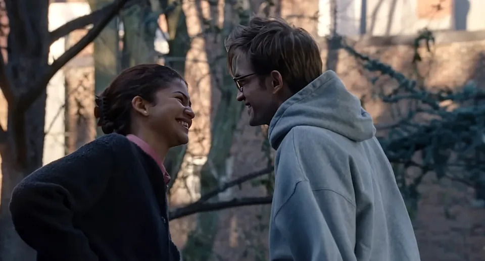 Two people outside smiling at each other closely, wearing casual clothing