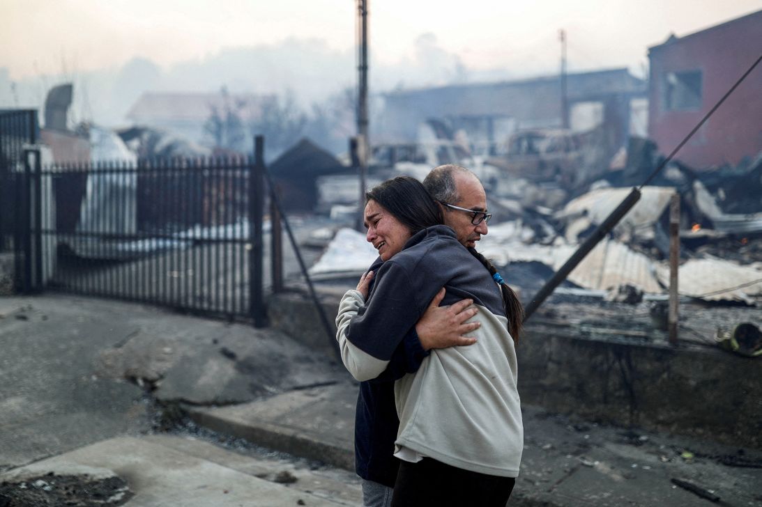 People embrace in front of burnt buildings in the aftermath of a forest fire in Concepción, Chile, January 18, 2026.