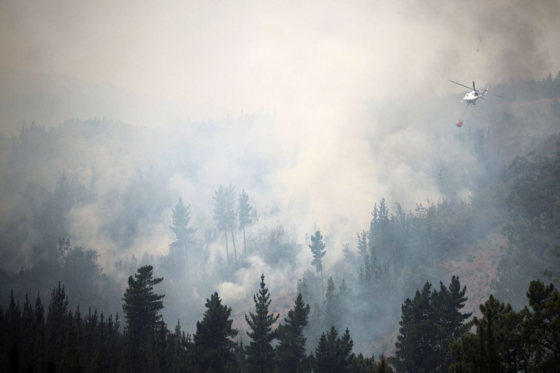 A helicopter tackles a forest fire in the Biobío region, where multiple wildfires prompted emergency evacuations in Chile on January 21, 2026.