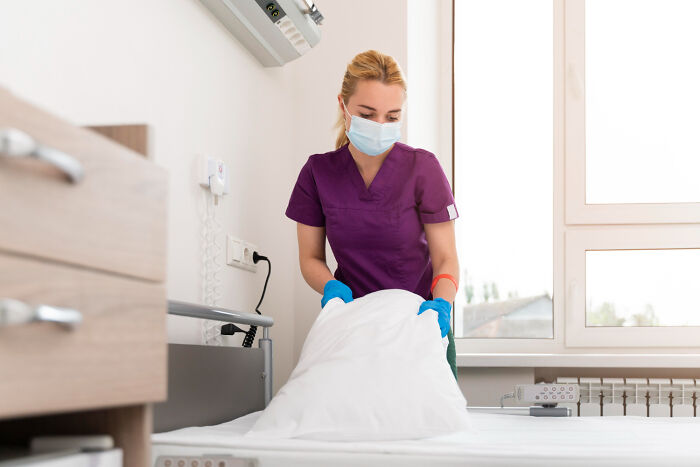 Nurse wearing mask and gloves making a hospital bed, illustrating hidden truths about hospitals and patient care.