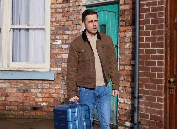 24_04_coro_todd_01 Todd stands with a blue suitcase outside of No. 5 Coronation Street