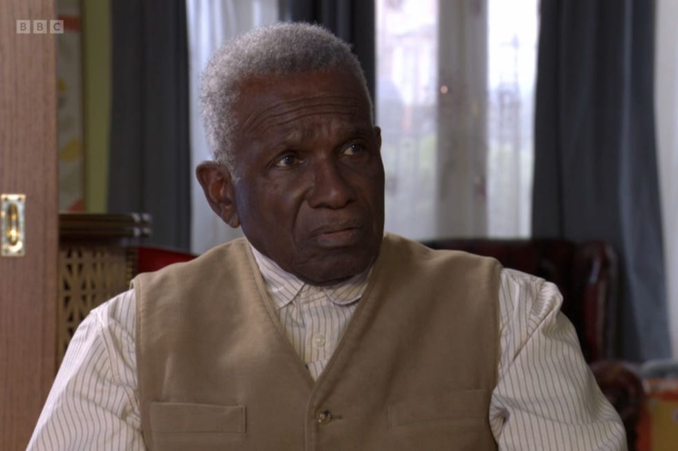 eastenders patrick trueman sitting down wearing a buttoned up vest over a shirt