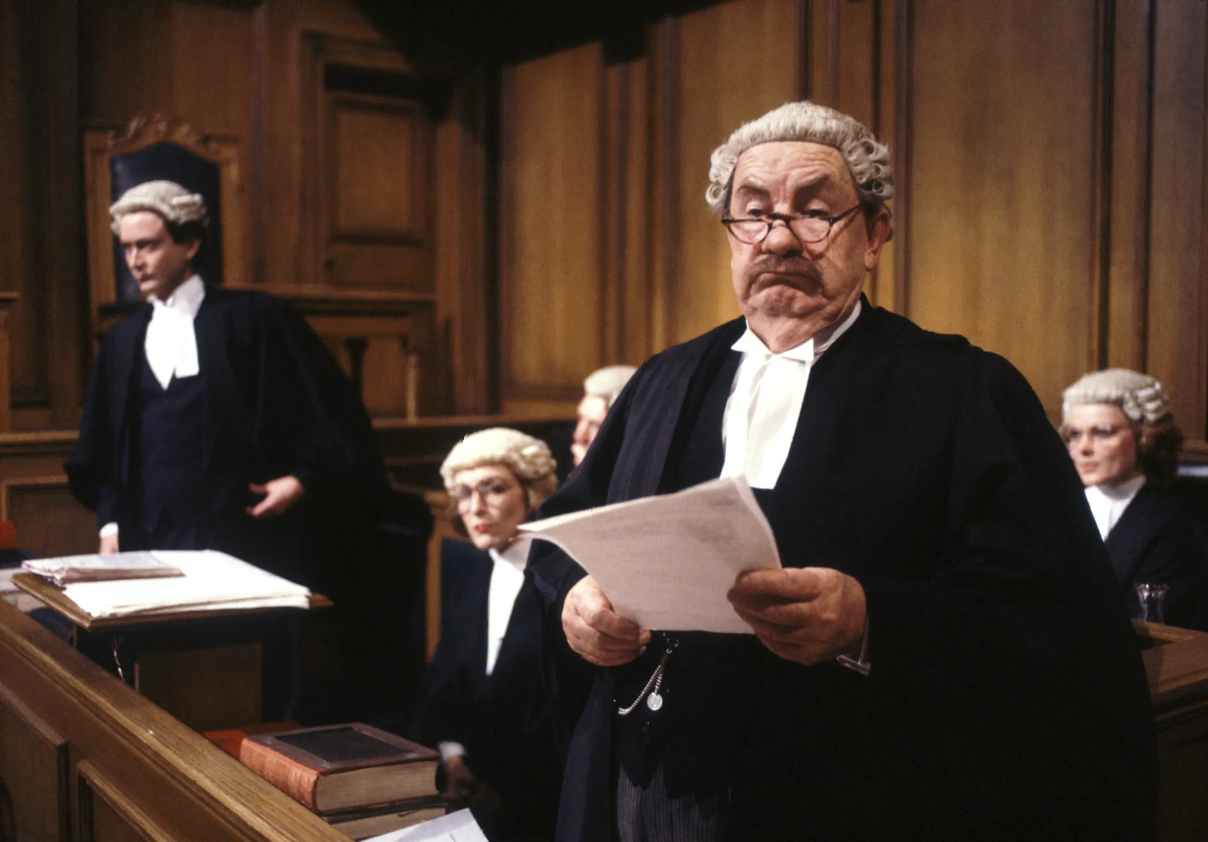 Leo McKern as Horace Rumpole in "Rumpole of the Bailey" holding papers in a courtroom.