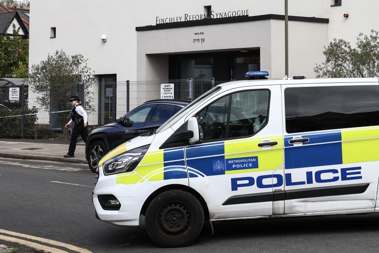 A police van parked in front of a gray and black building with signage reading FINCHLEY REFORM SYNAGOGUE.