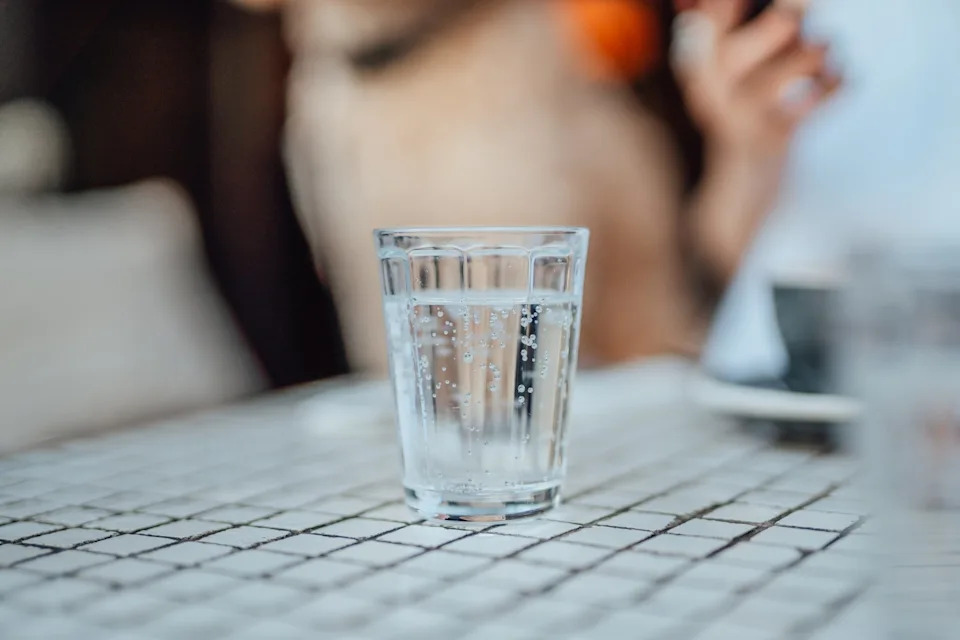 A glass of sparkling water sits on a checkered table, with a blurred background suggesting an outdoor setting