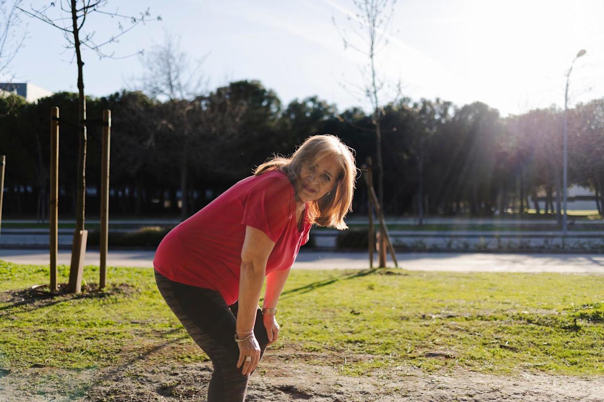 senior woman in a red shirt has shortness of breath so must pause her workout