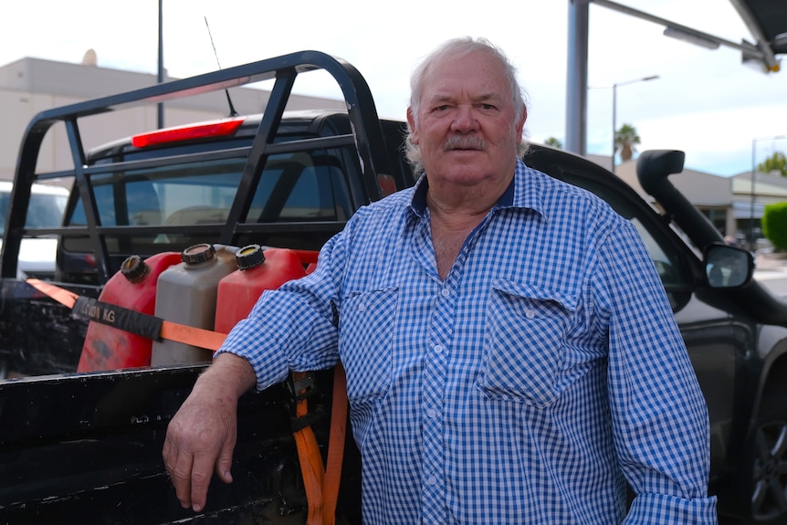 A man leans against a ute that has fuel cans in the back.