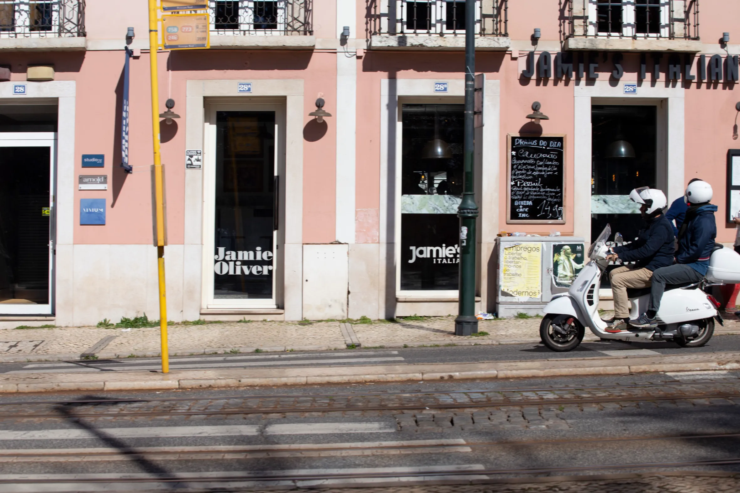 Two people on a scooter pass Jamie's Italian restaurant in Lisbon, Portugal.