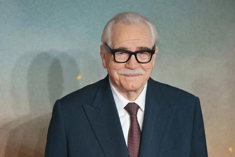 Brian Cox in a suit and glasses on the left, Jeremy Strong in a light green suit on the right.