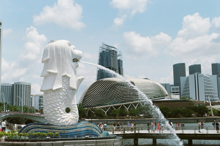 People walk on a pier in front of Singapore's merlion statue and the city's skyline