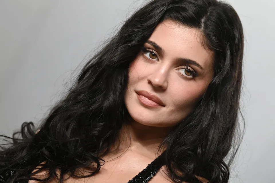 Kylie Jenner with long hair looks towards the camera, wearing an outfit with a delicate design