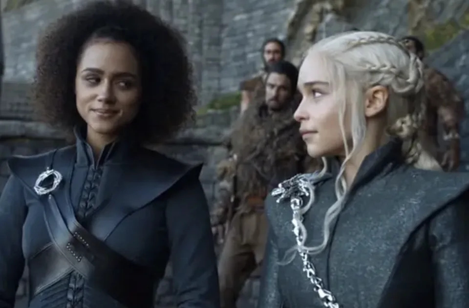 Nathalie with curly hair and Emilia with braided hair, wearing detailed medieval-style clothing, standing outside