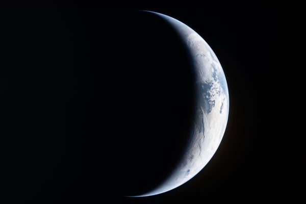 A deep-space view of Earth in crescent phase.