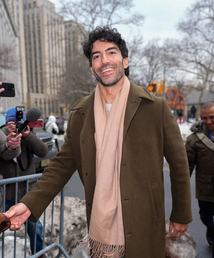Person smiling outdoors in winter attire, wearing a long coat and scarf, amid a small crowd