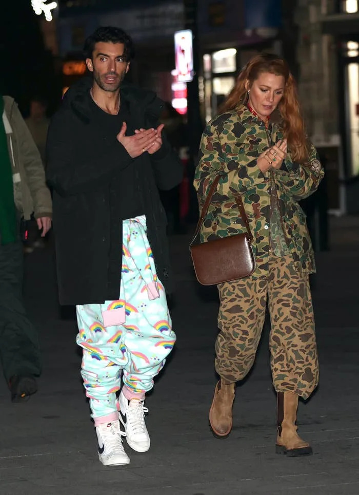 Two people walking outdoors. The person on the left wears a black coat and colorful pants, while the person on the right wears a camouflage jacket and pants