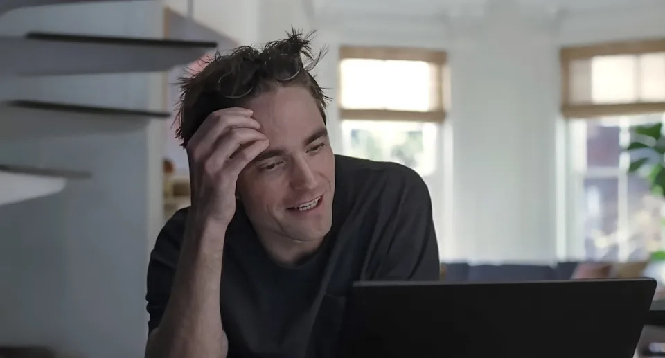 A person at home, sitting and smiling while looking at a laptop screen, seemingly engaged in a video call or online content