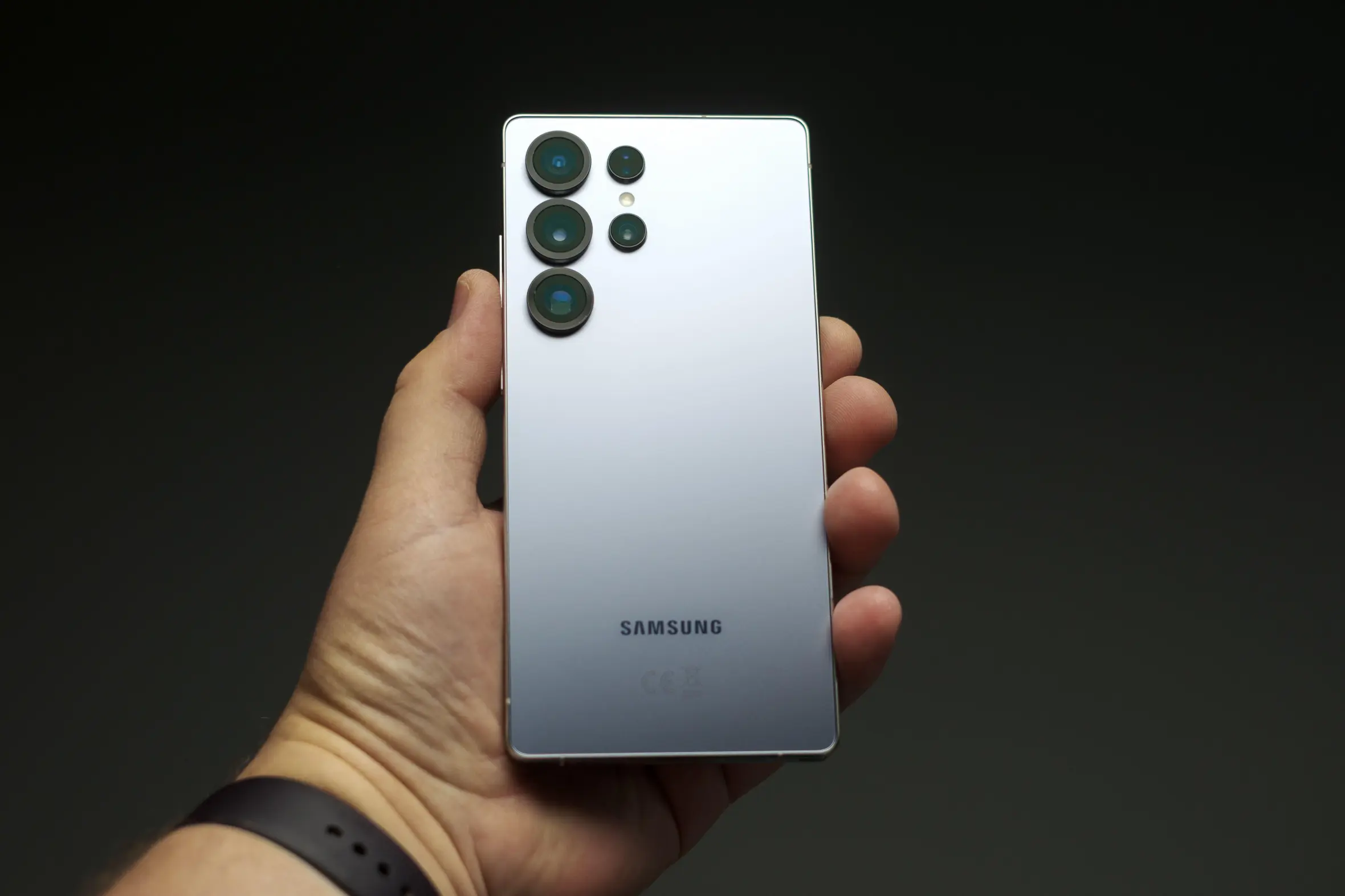 A hand holding the back of a silver Samsung Galaxy S25 Ultra smartphone, showcasing its multiple camera lenses.